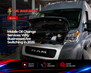 A gray RAM ProMaster cargo van sits inside a large commercial repair facility with its hood open for maintenance. The clean, well-organized workshop features high industrial ceilings, bright overhead lighting, tool carts, and a branded mobile truck repair van in the background. The scene highlights professional fleet vehicle service and repair operations in a modern automotive shop.